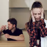 Мужчина пьет на кухне, женщина держится за голову